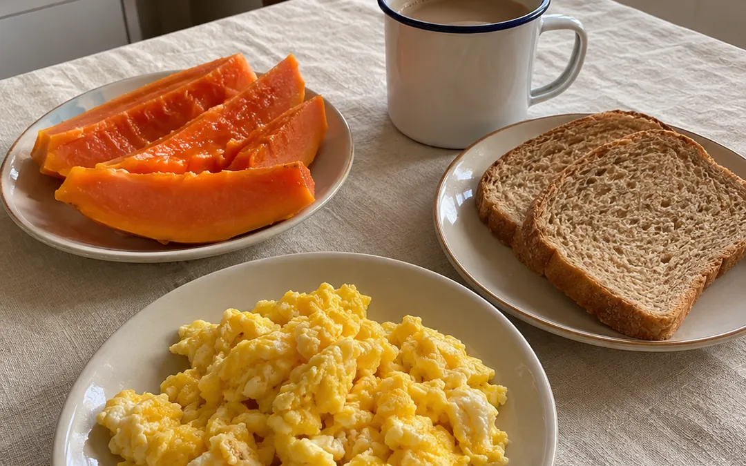 Mesa de café da manhã com ovos mexidos, mamão, pão integral e café com leite